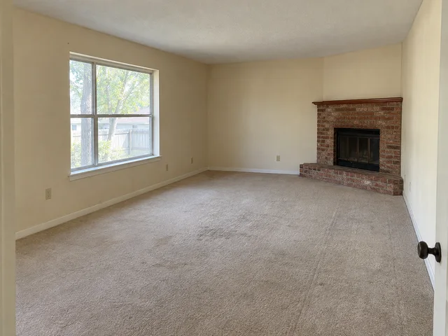 A dated living room with faded walls and worn carpet around a brick fireplace.